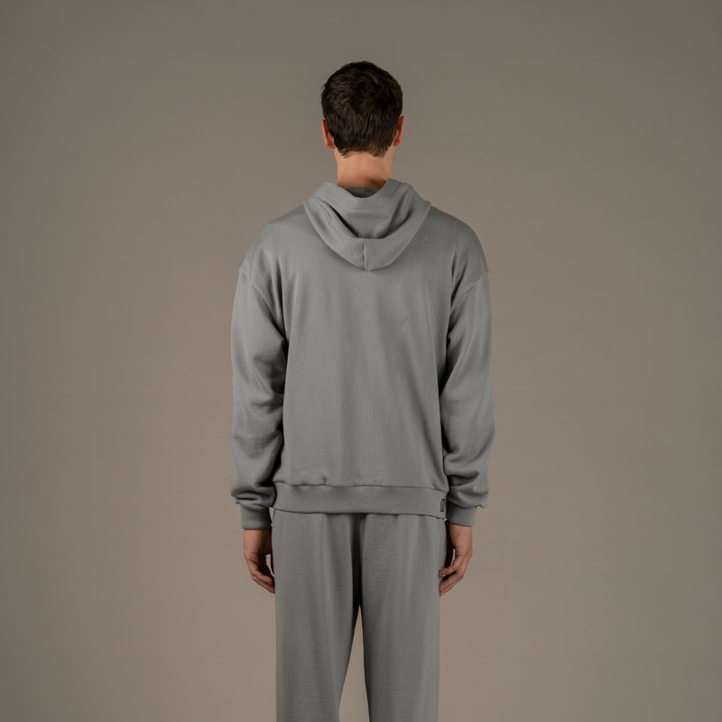 Model wears superior wool loungewear hoodie color grey, back.