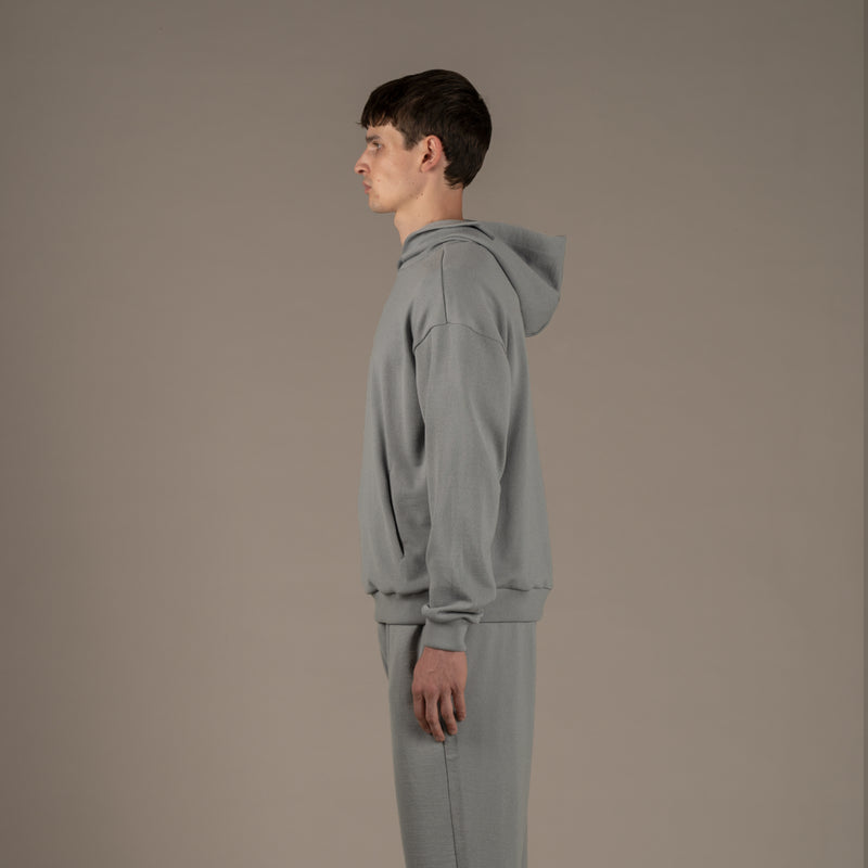 Model wears superior wool loungewear hoodie color grey, side.